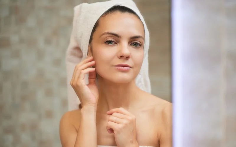 visage de femme avec une serviette sur les cheveux dans le miroir de sa salle de bain