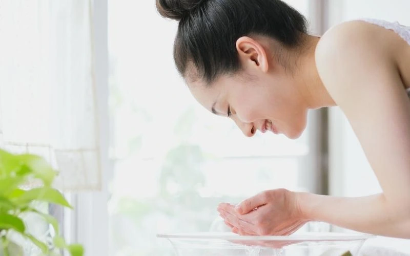 femme qui applique de l'eau sur son visage pour réparer sa peau après l'été